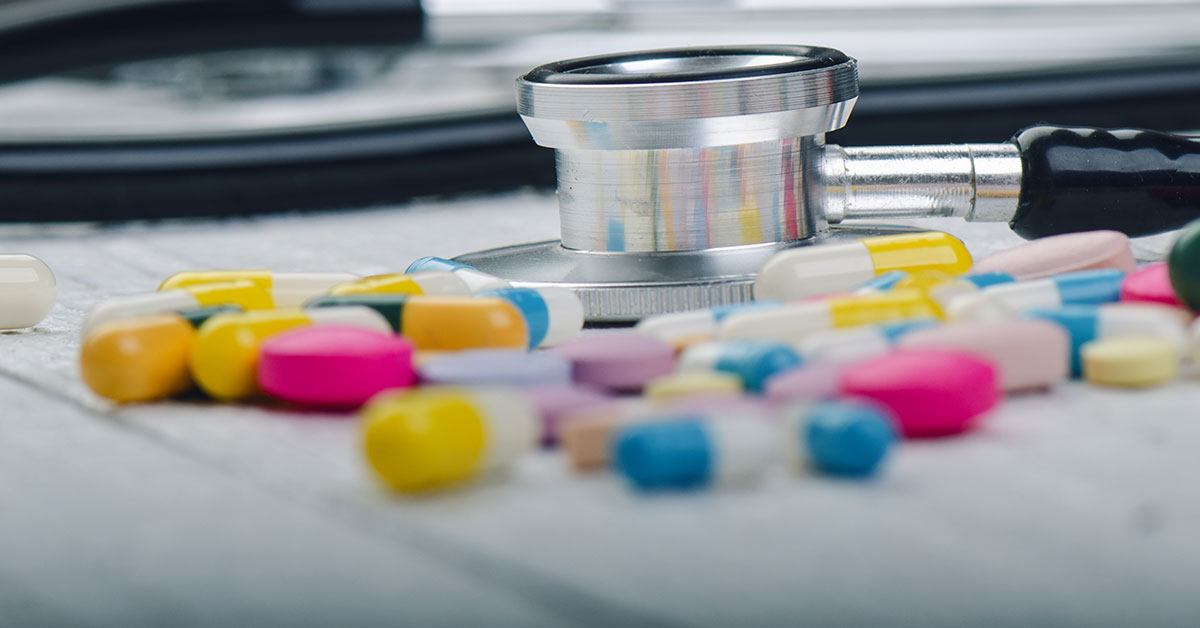 A stethoscope on a desk surrounded by numerous pills
